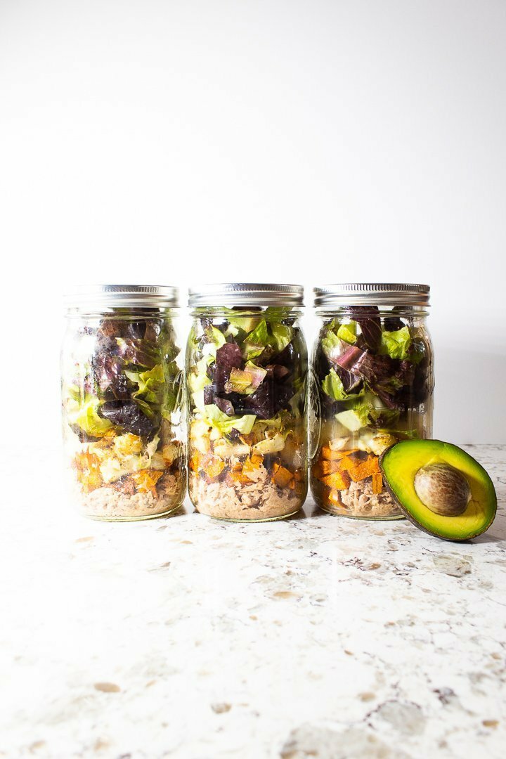 Mason jar salads of AIP Nourishing Buddha Bowl with sweet potato, cauliflower, chopped romaine, salmon, fermented kraut, avocado and arugula pesto.