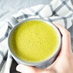 Hand reaching for Easy Coconut Milk Matcha Latte in a mug.