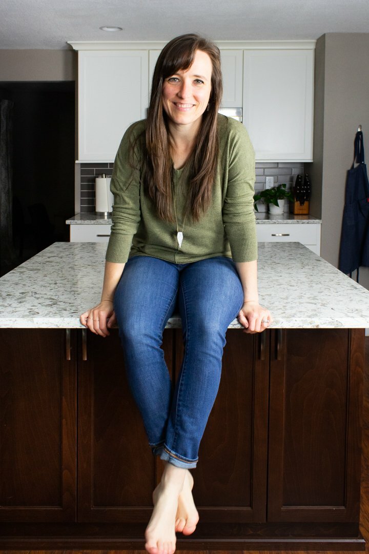 Andrea, the Hurried Health Nut, sitting on the counter in jeans and a sage green sweater.