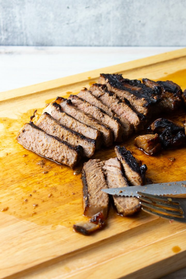 Sliced grilled balsamic steak on a wood cutting board.