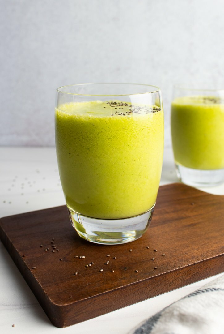Mango Matcha Smoothies on a wood serving board with a grey background.